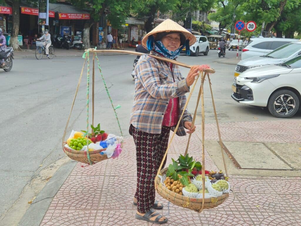 Vendeuse vietnamienne portant des paniers de fruits dans une rue